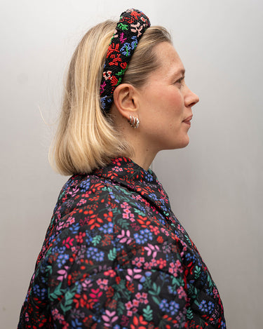 Modell iført en svart hårbøyle med røde, grønne, blå og rosa blomster på. Hårbøylen er laget av perler.