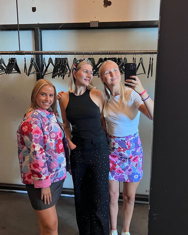 Tre jenter som tar et bilde i speilet iført Charlotte-jeans, Kristin quiltjakke og Kristin quiltskjørt fra DAAE Studio.